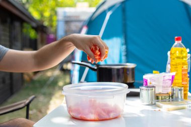 Tanımlanamayan bir adam masada oturuyor plastik kaseye domates ekliyor ve kamp alanında salata hazırlıyor.