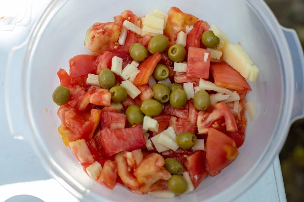Top view of tomato salad with olives and cheese served in bowl on sunlit table during picnic