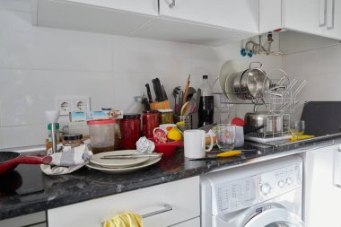 Boş bulaşıklarla dolu kirli bir tezgahı ve temizleme ve depolama kavanozları olan bir evin mutfağı.