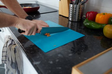 Anonymous person cutting carrots on a blue board, while the vegetables are poached in the pan