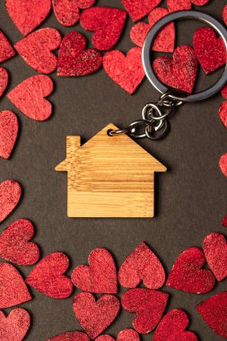Top view of a composition of a keyring with a charming little wooden house placed among small red decorative hearts on a brown surface