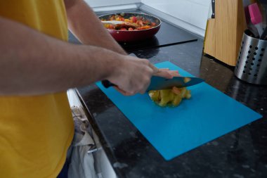 Anonymous person slicing a tomato on a blue board in the kitchen