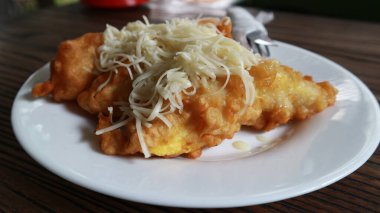 Pisang Goreng Keju ya da kızarmış muz peyniri beyaz tabakta çedar peyniri rendesiyle servis edilir..