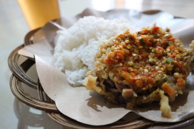 Ayam Geprek. Popüler bir Endonezya yemeği, limon yaprağı biber soslu kızarmış tavuk, pilav ve pirinç kağıdıyla kaplı buzlu çay..