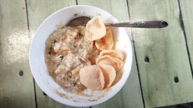 Yakın plan Bubur Ayam veya doğranmış tavuk, kek, kızarmış soya fasulyesi, kraker, kereviz, taze soğan ve yumurtayla karıştırılmış tavuk lapası..