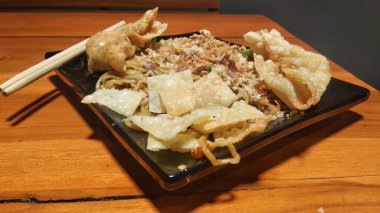 Jakarta, Endonezya - Ekim 06, 2022: Tavuklu erişte, kızarmış hamur köftesi, dilimlenmiş tavuk ve siyah tabakta kızarmış soğan serpiştirilmiş. Asya tarzı yemekler.