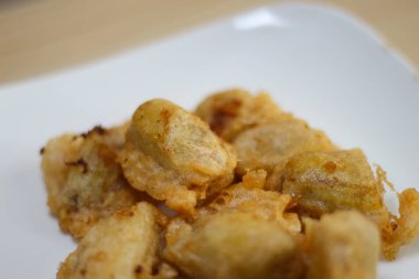 Yakından bakınca Pisang Goreng Keju ya da kızarmış muzu beyaz tabakta ahşap masada görebilirsiniz..