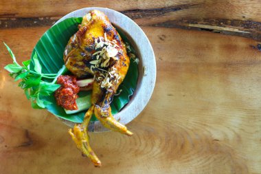 Tavuk gourami ya da ızgara tavuk ya da ahşap masada kızarmış soğan üzerine sebze ve acı biber sosu (sambal) ile Ayam bakar.
