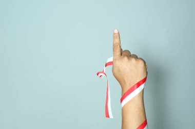 Arka planda boş kopya alanı olan kırmızı ve beyaz bir kurdeleyi tutarken yumruğu olan ve kelimeleri işaret eden bir adam. Endonezya Bağımsızlık Günü konseptini temsil etmek