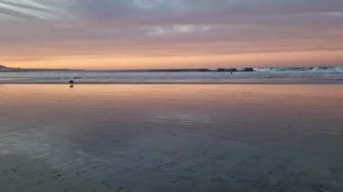 Famara Sahili 'nde gün batımının nefes kesici güzelliğini tecrübe et, Lanzarote. Güneş ufkun altına batarken, gökyüzü sıcak renklerden oluşan bir tuvale dönüşür, engebeli uçurumlara ve sakin Atlantik sularına altın bir parıltı saçar.. 
