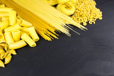 Dry pasta on black wooden background with space for text clipart