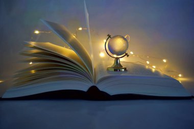 Parlak ışıklı cam küresi olan açık bir kitap.