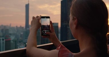 Turist kadın, Malezya 'nın başkentinde gün batımında gökdelenlerin fotoğrafını çekiyor. Bir apartmanın çatısından bulutlu şeftali rengi gökyüzü manzaralı. Sadece dikiz aynası. Tatil