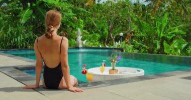 Kahvaltıda bir bardak portakal kokteyli ile havuz kenarında dinlenen bir kadın. Güneş banyosu yapan yalnız bir kız. Tatil tatili konsepti. Sağlık ve güzellik. Yeşil doğa geçmişi. Bali Adası