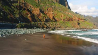 Hava manzaralı siyah volkanik kum plajı. Anaga sıradağları, Tenerife 'nin yeşil kuzey kıyıları, Kanarya Adaları, İspanya, Avrupa. Kardiyo çalışması. Sabah koşusu. Mavi okyanus dalgaları köpürüyor.