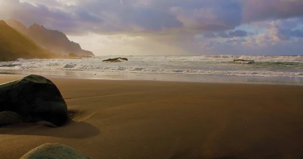 Atlantik Okyanusu kıyısında suyun buharlaşması, köpüklü dalgalar. Güneşli sabahın erken saatlerinde. Tenerife adasındaki boş siyah kumsal. Rahatlama ideal görüş. Kanaryalar