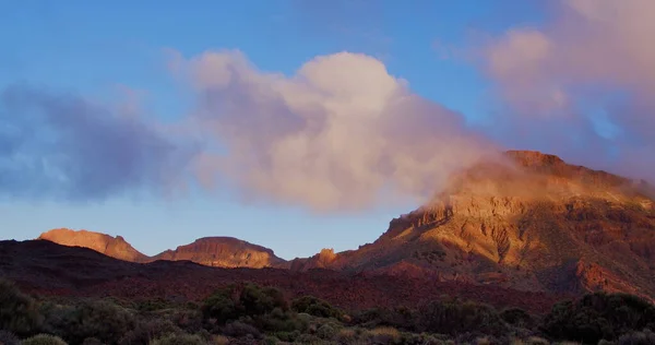 Range of mountain at sunset, clouds above Teide National Park in Tenerife, Canary Island, Spain. in the foreground local bush cacti and other desert vegetation.