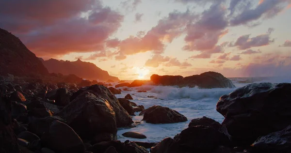 Tenerife. Denizin üzerindeki kayalık sahilde turuncu gün batımı. Güneşin renkli ışınları ve gün batımında parlayan dramatik bulutlar. Kimse..