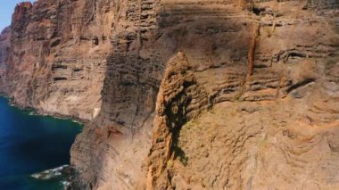 Tenerife Adası 'ndaki Los Gigantes kayalıkları boyunca insansız hava aracı uçuşu. İspanya. Mavi okyanus suları. Çorak dağ sıraları. Cennete, muhteşem volkanik plaja git. Güneşli bir gün. Her yere git
