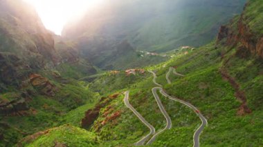 Tropikal bir ormanın dağlarındaki dolambaçlı bir yolun üzerindeki hava manzarası. Masca Vadisi ve vadideki küçük bir köy. İlkbaharda yeşil manzara. Tenerife Kanarya Adaları İspanya Avrupa. Seyahat