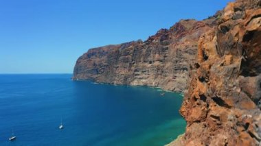 Tenerife Kanarya Adası 'ndaki taş sahil şeridi. Havadan çekilen yavaş çekim, Los Gigantes 'in okyanus kayalıklarını ortaya çıkarıyor. Deniz kıyısındaki yüksek kayalık dik dağlar. Donmuş volkanik lav. Jeolojik