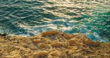 Fuerteventura uçurumu kıyısında Roque del Morro ve kumtaşları ön planda. Gün batımında kayalık kireçtaşlarına okyanus dalgaları sıçrıyor. Su yansıması. Gün batımının yumuşak ışığı. Kanarya Adaları. İspanya