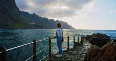 Gün batımında fırtınalı okyanusun tadını çıkaran bir kadın. Tenerife Adası 'nın kuzeyindeki Kanarya adasının volkanik dağları. Güzel deniz manzaraları.