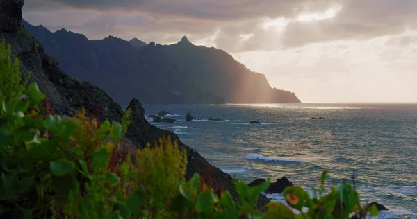 Dramatik bulutlu gün batımı gökyüzü. Güneş ışınları derin okyanusa batmadan önce kara bulutların içine sızar. Güneş ışığı dağ silueti. Kimse..