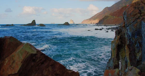 Waves break on rocks in a blue ocean. Sea waves on beautiful beach, waters crashing against an empty stone rock cliff. Canary island, Tenerife. Sunset.