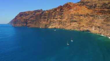 Güneşli bir günde derin mavi Atlantik Okyanusu 'nda kayalıkları olan deniz manzarası. Tenerife Kanarya Adası 'ndaki sakin su ve Los Gigantes uçurumlarının muhteşem manzarası. Hava manzarası. Birkaç beyaz gemi var.