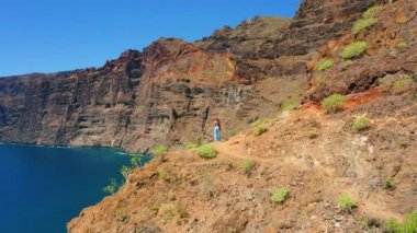 İnanılmaz büyük kayalıkları olan okyanus suyu Los Gigantes uçurumları ve turist kadın siluetinin arka manzarası dağ yamacında duruyor. Tenerife Kanarya Adaları. Güneşli bir günde hava aracı deniz manzarası. Seyahat