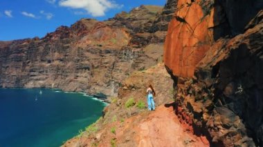 Turist kadın silueti dağ yamacında duruyor ve Los Gigantes uçurumları Tenerife Kanarya Adaları 'ndaki inanılmaz kayalıklarla okyanus suyunun tadını çıkarıyor. Güneşli bir günde deniz manzarası. İspanya 'ya seyahat