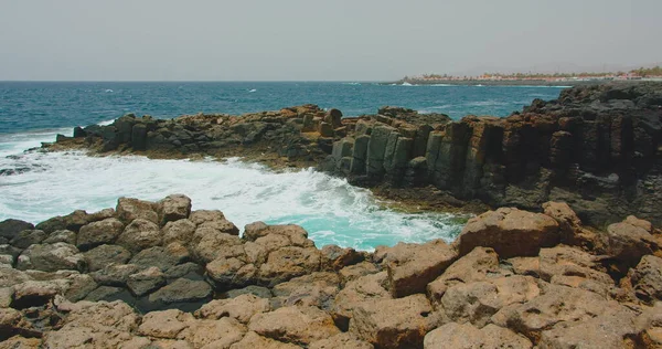 Okyanus dalgaları boş kayalık siyah plaja çarpıyor. Mavi deniz suyu kıyı şeridini kırıyor. Volkanik taşlara yakın, yavaş çekimde su sıçrayan kıyılar. Kimse..