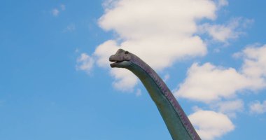 Park cazibe merkezi. Hareket halindeki bir dinozor kafası. Mavi gökyüzü arka planında taş devri canavarı figürü. Kimse..