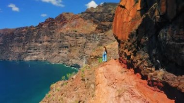Volkanik kayanın kenarında duran turist kız siluetinin arka görüntüsü ve Los Gigantes 'in devasa uçurumları Tenerife Kanarya Adaları ile okyanus manzarasının keyfini çıkarmak. Güneşli bir gün. Yalnız kadın İspanya 'ya gidiyor.