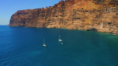Güneşli bir günde derin mavi Atlantik Okyanusu 'nda kayalıkları olan deniz manzarası. Tenerife Kanarya Adası 'ndaki sakin su ve Los Gigantes uçurumlarının muhteşem manzarası. Hava manzarası. Birkaç beyaz gemi var.