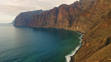 Los Gigantes 'teki granit uçurumların üzerindeki hava aracı görüntüleri. Derin mavi Atlantik Okyanusu 'ndaki dev kayalar. Kanarya Adaları, İspanya. Avrupa. Gün batımında sakin yaz havası. Dağların tepesinde sisli sis