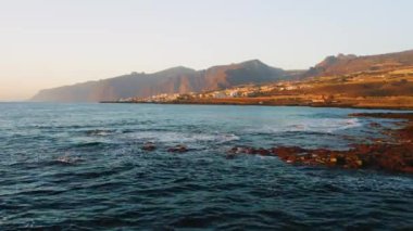 Havadan. Volkanik kayalık plajı. Okyanus sakin dalgalar şeffaf su. Dünyayı keşfetmek. Tenerife. İspanya 'daki Kanarya Adaları. Güzel bir şehir tatil köyü. Seyahat bağımlısı. Gün batımı