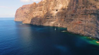 Küçük beyaz yatlar okyanusta büyük Los Gigantes uçurumlarının arka planında yüzüyor. Tenerife, İspanya. Kayaların üzerinden uçmak. Sakin derin deniz sularının muhteşem manzarası. Cennete yolculuk