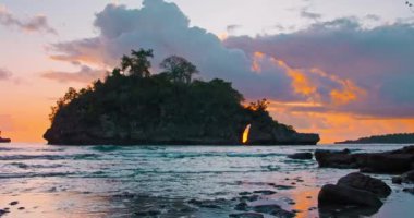 Nusa Penida Adası 'nda turuncu gün batımında sakin okyanus dalgalarıyla tropik Crystal Bay Sahili. Denize tuzlu su sıçratma, içinde delik olan sudan çıkan kaya. Statik görüş. Güneş ışığının yansıması