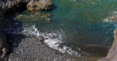 Terkedilmiş siyah volkanik bir plajın üst manzarası. Tenerife adasının kıyısında. Deniz dalgalarının kıyıya ulaştığı görüntüler. Hiç kimse. Rahatla video.