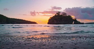 Crystal Bay Beach Nusa Penida arka planda güzel günbatımı. Turuncu ışık su yüzeyine yansıyor. Sakin okyanus dalgaları kumlu kıyıya çarpar. Sabit çekim yavaş çekim. Kimse..