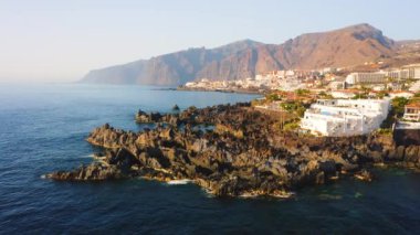 Tenerife 'deki eski bir kasabanın üzerinde havadan görüntülü insansız hava aracı uçuşu. Eski bir deniz kenti Puerto de Santiago. Volkanik bir Kanarya Adasının kıyısındaki yazlık evler. İspanya. Mavi derin okyanus