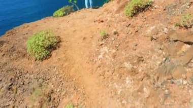 İnanılmaz büyük kayalar ve turist kadının dikiz manzaralı havadan okyanus manzarası. Sahne açılır ve kamera yüzükoyun döner ve yavaş yavaş denize ve uçuruma doğru hareket eder. Tenerife Kanaryası