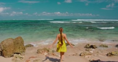 Okyanusa koşan çıplak ayaklı turist kadın Endonezya 'nın Bali Adası' ndaki kumlu yeşil bovling plajının tadını çıkarıyor. Yalnız kız, kollarını aç, ellerini kaldır, eğlen, deniz kenarında gülümse. Yakın plan. Dalgalar çarpar
