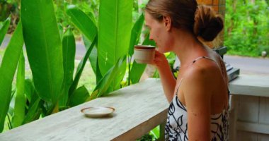 Kadın sabah sıcak Bali kahvesi içip yeşil bahçenin tadını çıkarmaya çalışıyor. Bali Adası Endonezya 'sındaki yalnız seyahat kızına yakın çekim.