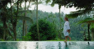 Tropik ormanların arasında yüzme havuzunun yanında yürüyen bir kadın. Yaz tatilindeki uzun saçlı kız. Palmiye ağaçları. Rahatla ve doğanın tadını çıkar. Hafta sonları turist. Tatil yeri refahı uyumu.