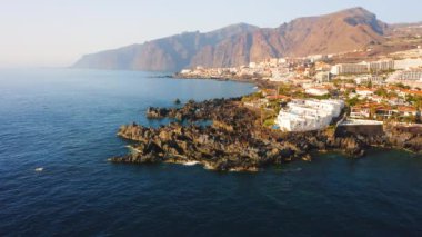Tenerife Adası sahil beldesinin havadan görünüşü. Puerto de Santiago del Teide 'ın kayalık volkanik sahildeki tatil evleri. Arka planda Los Gigantes uçurumları var. Kimse..