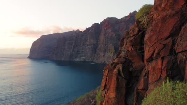 海の水の上にカラフルな夕日 波が岩の山のビーチフロントでクラッシュします 崖のシルエットの上に空の太陽を設定 熱帯の自然景観 パラダイス島テネリフェスペイン シネマティックドローン撮影 — ストック動画
