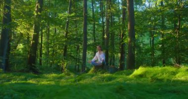 Ormanda yoga yaparak zihinsel hastalıkların tedavisi. Genç kız kütüğün üzerinde oturuyor ve ormanlık alanda meditasyon yapıyor. Güzel bir kadın Lotus pozisyonunda oturuyor ve akşam gözleri kapalı rahatlıyor.